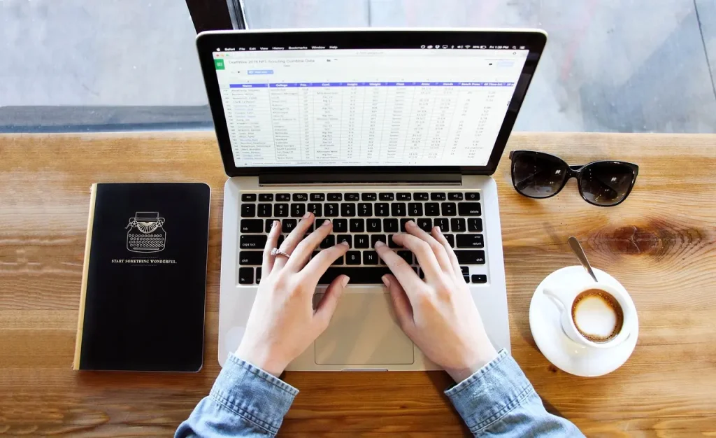 Typing on laptop with coffee and notebook nearby.