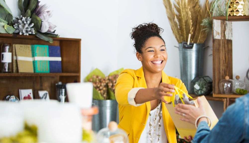 Smiling woman in yellow jacket hands over bag.