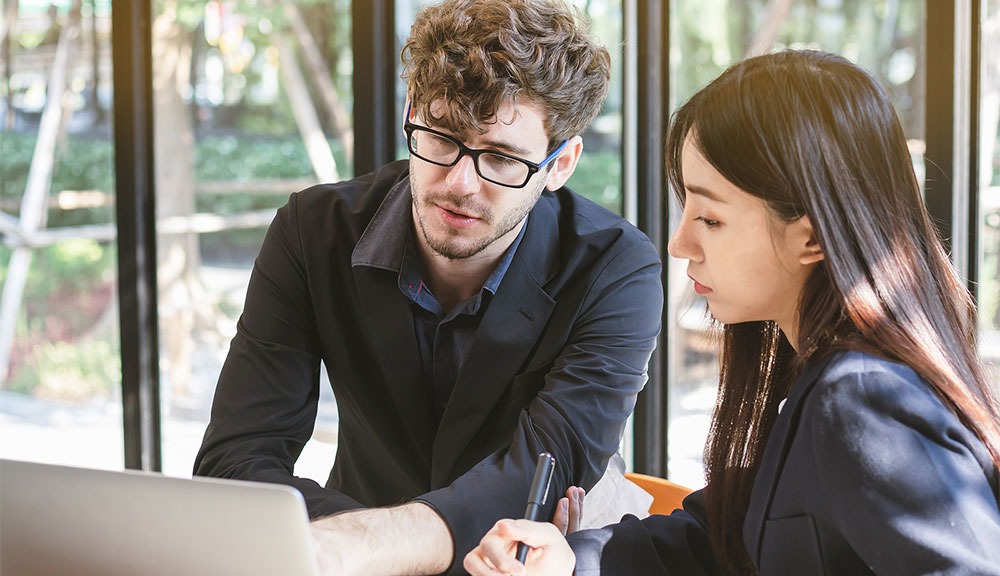 Two colleagues discussing work at a laptop.