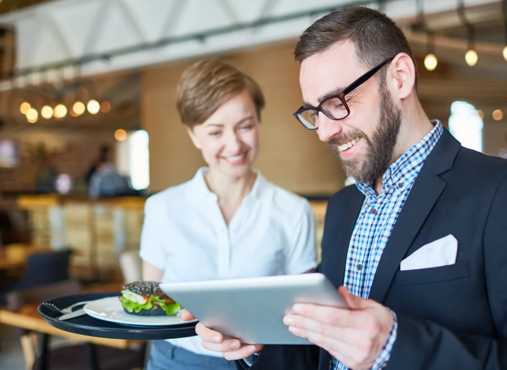 Man using tablet while waitress holds burger